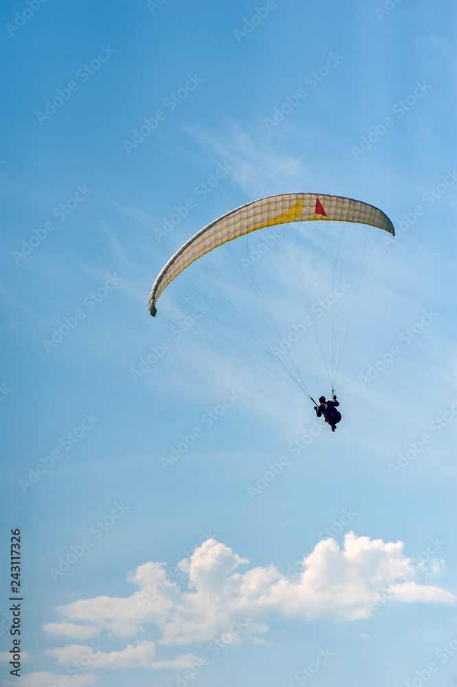 Alone paraglider flying in the blue sky against the background of clouds. Paragliding in the sky on a sunny day. Alone paraglider flying in the blue sky against the background of clouds. Paragliding in the sky on a sunny day.