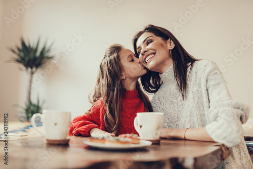 Daughter kissing her mama in cheek and smiling photo