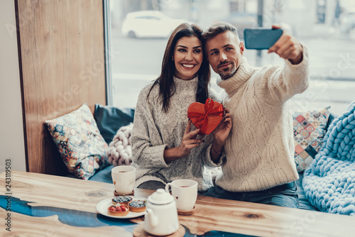 Two person sitting in cafe with present and making selfie photo