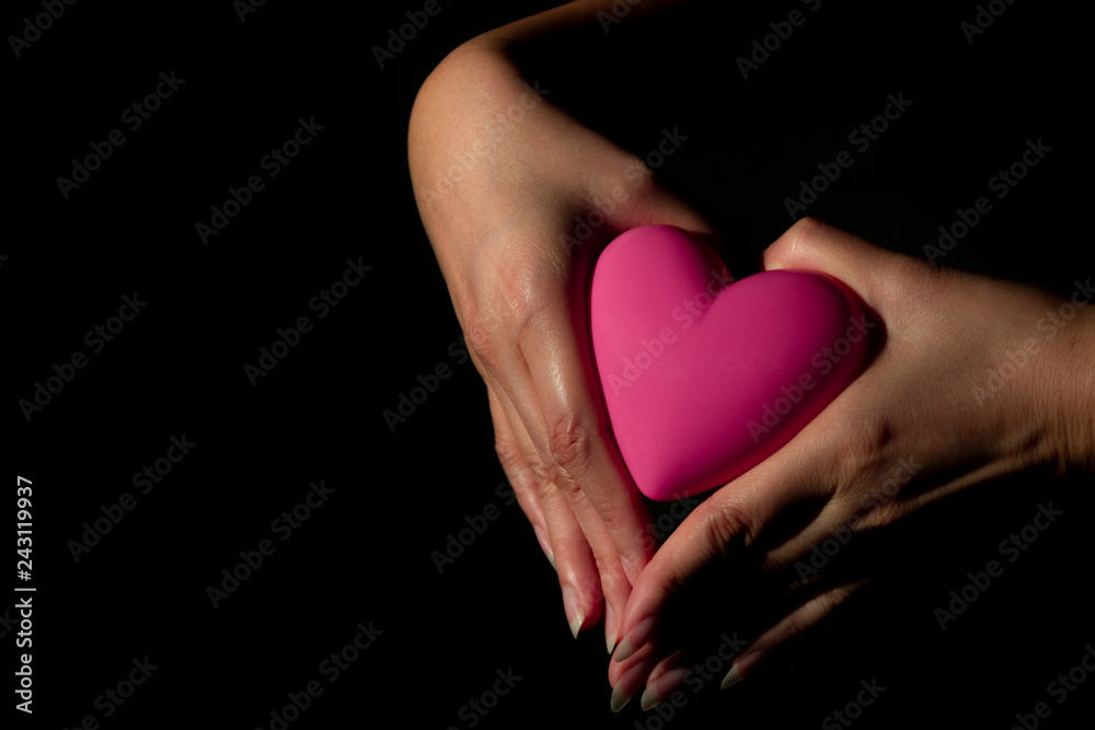 Female hands holding pink heart shape on a black background. Symbol, Human Hand Female hands holding pink heart shape on a black background. Symbol, Human Hand