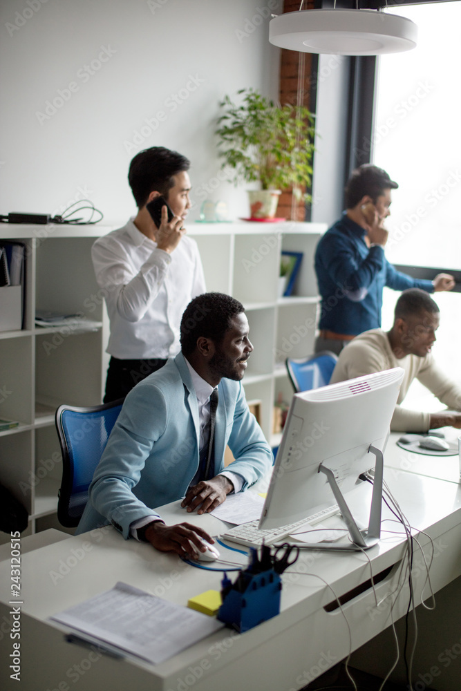 African american man working on his personal computer, surrounded by his colleagues in office.Handsome young man at his desk. African american man working on his personal computer, surrounded by his colleagues in office.Handsome young man at his desk.