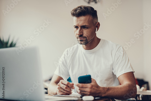 Man holding cellular and pen in hands and looking on laptop