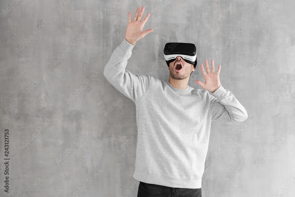 Excited handsome guy experiencing virtual reality while using VR headset for entertaining, standing against gray wall, touching something in the air with hands Excited handsome guy experiencing virtual reality while using VR headset for entertaining, standing against gray wall, touching something in the air with hands