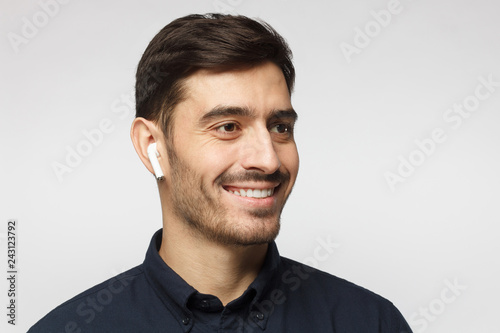 Close up headshot of young smiling business man wearing deep blue shirt, listeting to his favorite music track