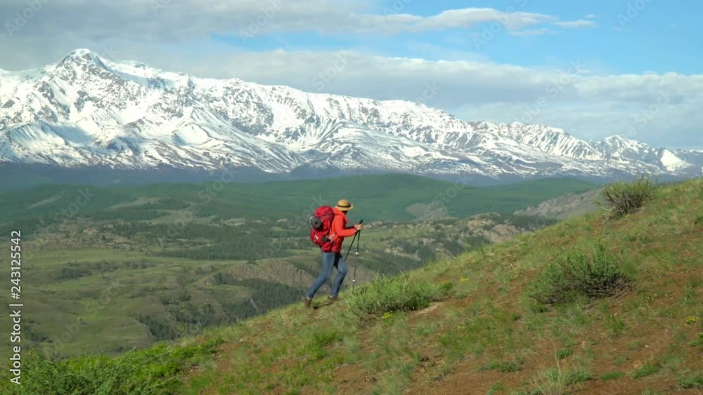 The woman the traveler with a red backpack rises by the mountain, looks at snow mountains. The woman the traveler with a red backpack rises by the mountain, looks at snow mountains.