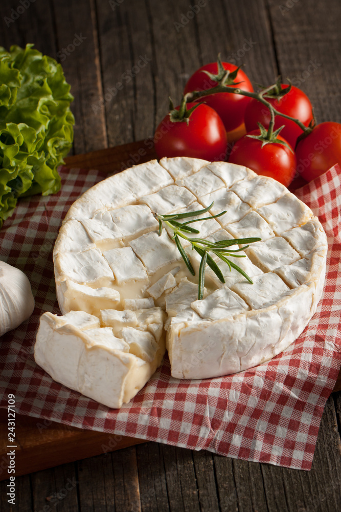 Camembert and brie cheese on wooden background with tomatoes, letuce and garlic. Italian food. Dairy products. Camembert and brie cheese on wooden background with tomatoes, letuce and garlic. Italian food. Dairy products.
