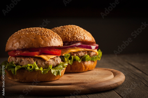Home made hamburger with beef, onion, tomato, lettuce and cheese. Fresh burger close up on wooden rustic table with potato fries, beer and chips. Cheeseburger.