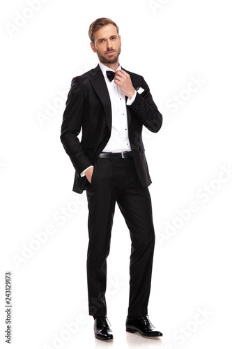 relaxed businessman in black suit fixing his bowtie while standing