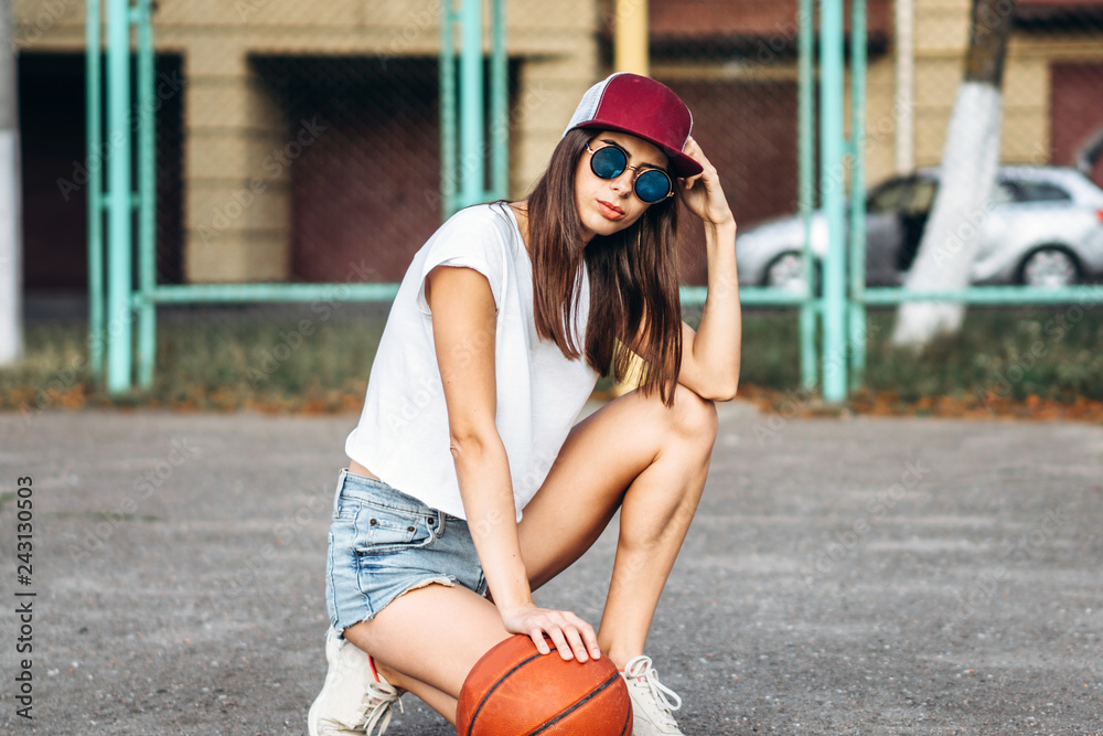 Pretty young sporty girl with basketball ball outdoor.