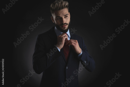 portrait of businessman arranging red tie and looking to side