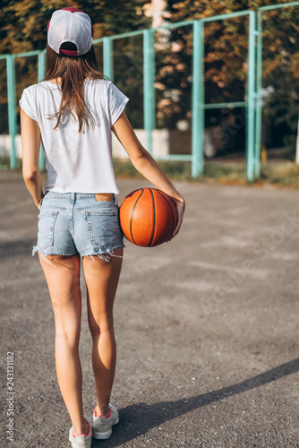 Pretty young girl holding basketball ball, rear view.