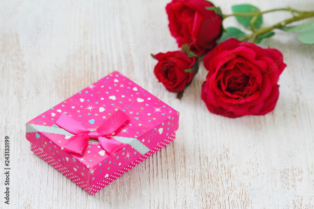 Fresh red roses and gift box on wooden table