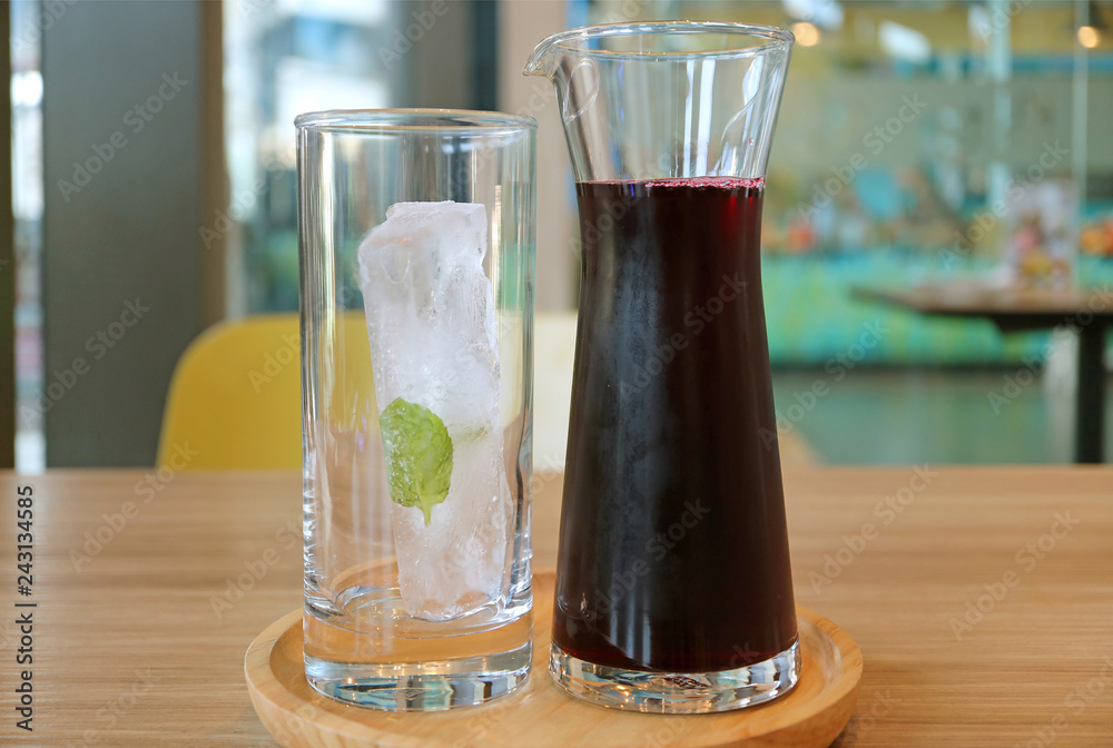 A Carafe of Roselle Juice with a Glass of Ice Cube on Wooden Tray Served on Wooden Table A Carafe of Roselle Juice with a Glass of Ice Cube on Wooden Tray Served on Wooden Table