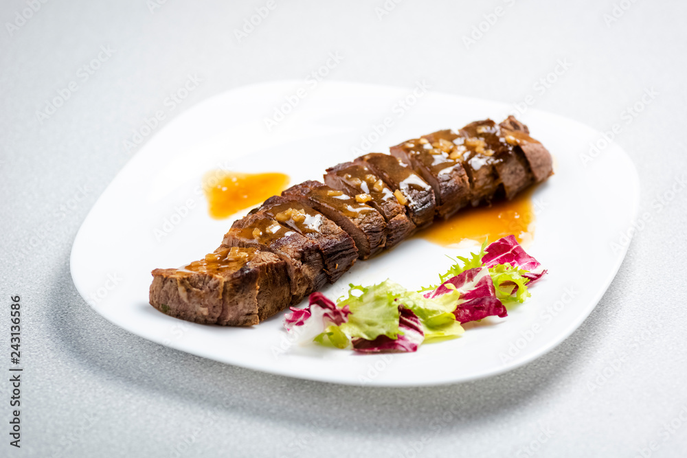 a sliced steak poured with onion decorated with lettuce leaves a sliced steak poured with onion decorated with lettuce leaves