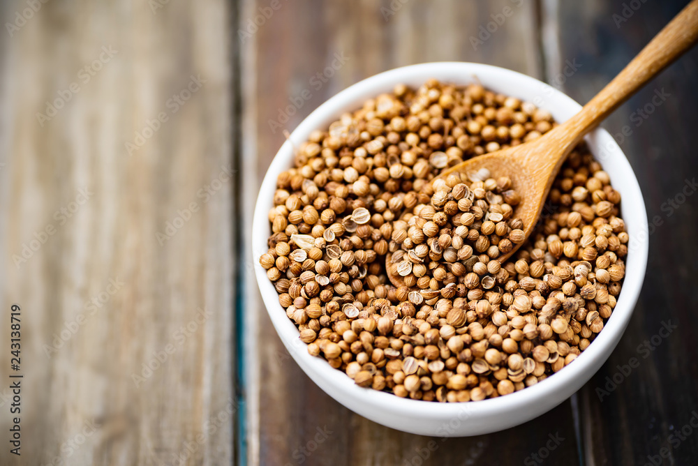 Dried coriander seeds in a bowl with wooden spoon on wooden table, herbs and spices, food ingredients Dried coriander seeds in a bowl with wooden spoon on wooden table, herbs and spices, food ingredients