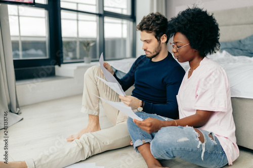 Fotografi African and Caucasian mixed race married couple sitting on the floor at home checking unpaid bills, taxes, due debt, bank account balance