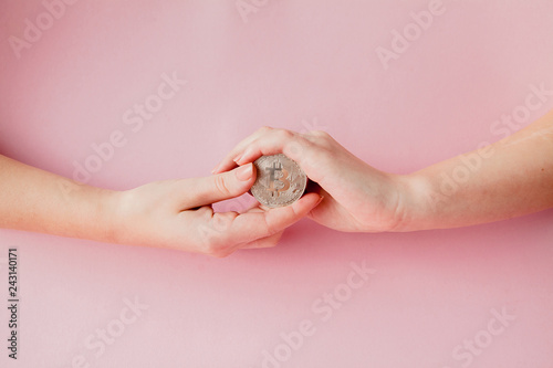 Woman's hands holding bitcoin on a pink background, symbol of virtual money