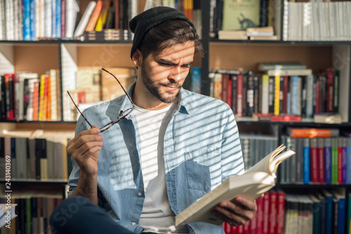 Male student sitting on a chair and with book in one hand and eyeglasses in other.