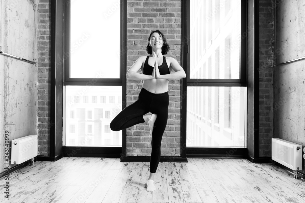 cheerful motivated woman is standing on one leg and practising yoga. black and white photo.motivation and health care cheerful motivated woman is standing on one leg and practising yoga. black and white photo.motivation and health care
