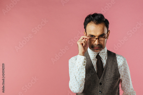 Portrait of a mature man in brown vest holding his glasses, isolated on black studio background