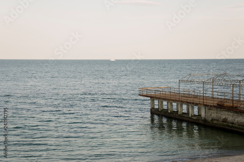 Black Sea. Water with no waves and little boat far away. Big stone in front. Calm. Mainly cloudy weather. Blue and grey color. Before rain 