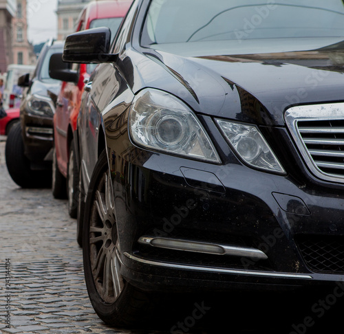 Close-up headlight of black modern car with other cars on background © volody10