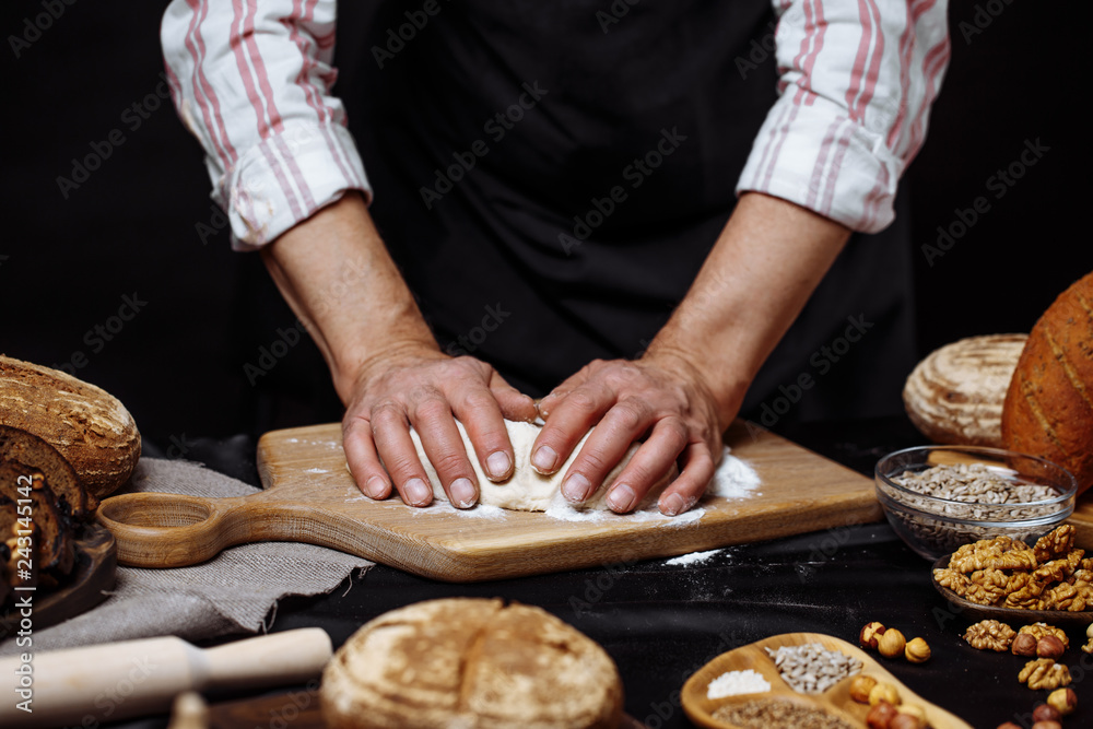 Hands of male chef cook working with dough, surrounded by bread and long loafs from whole wheat flour. Bakery concept. Homemade bakery concept Hands of male chef cook working with dough, surrounded by bread and long loafs from whole wheat flour. Bakery concept. Homemade bakery concept
