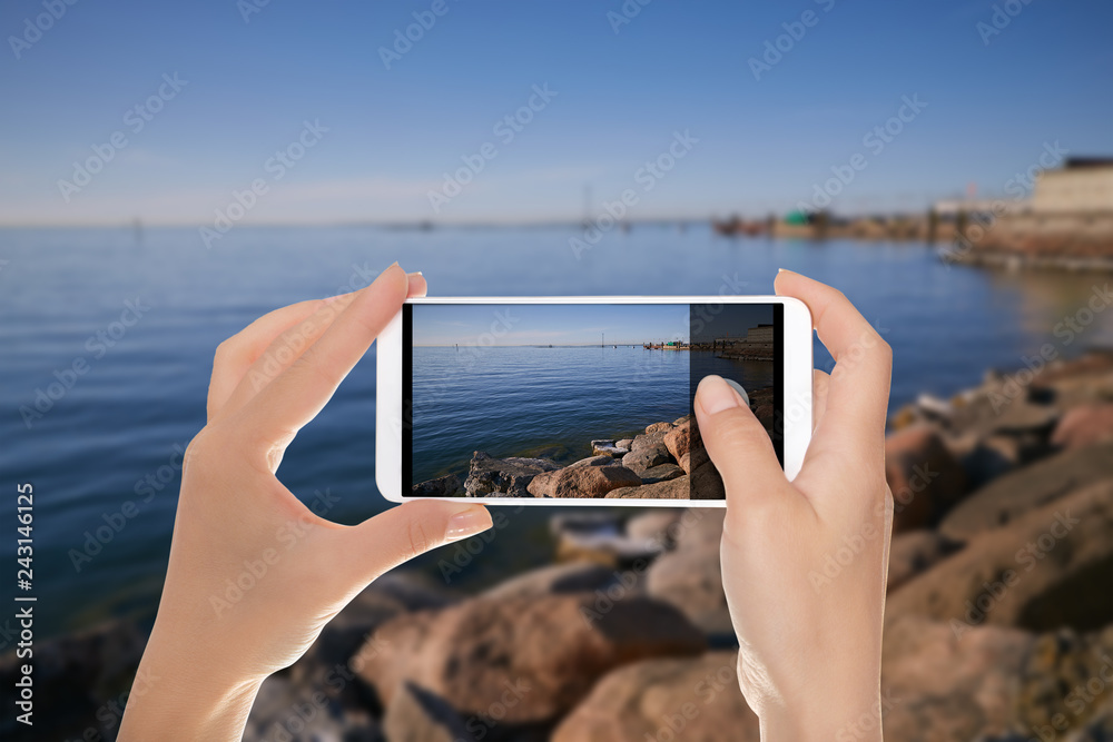 A tourist is making a photo of the embankment on the Baltic Sea in Tallinn on a clear summer evening on a mobile phone