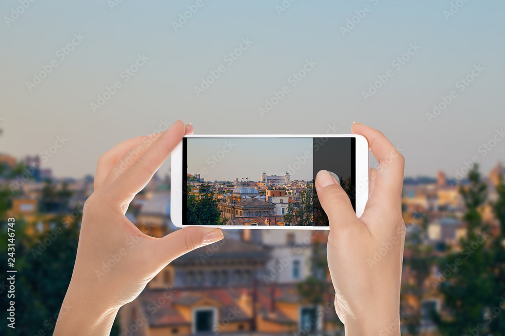 A tourist is making a photo of morning panorama of Rome with a view of the Vittoriano monument on a mobile phone
