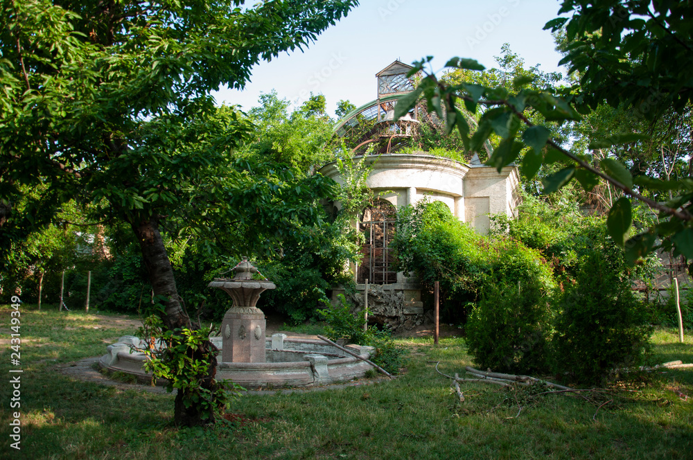 Old ancient white destroyed stone house on the green yard with trees around. Poverty and misery, South, summer 