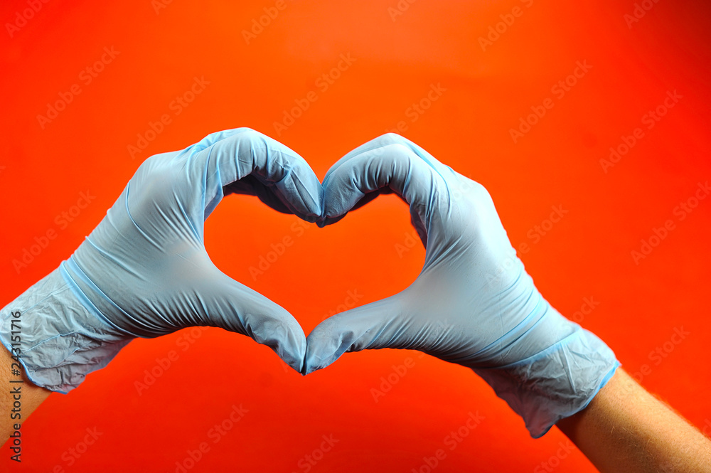 Obraz premium Hands in medical latex gloves. Hands form a heart shape. The gesture symbolizes the declaration of love. Red background. Close-up. Concept: Hand gestures for expressing emotions. Macro shooting.