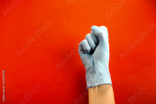 Hand in medical latex glove. Hand clenched into a fist. Red background. Close-up. Concept: Hand gestures for expressing emotions.
