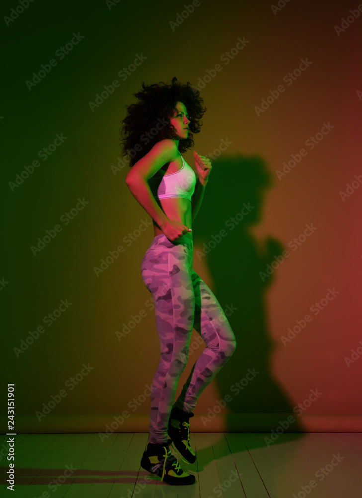 Full length young sport woman with afro hairstyle running jogging in gyn green and pink neon light Full length young sport woman with afro hairstyle running jogging in gyn green and pink neon light