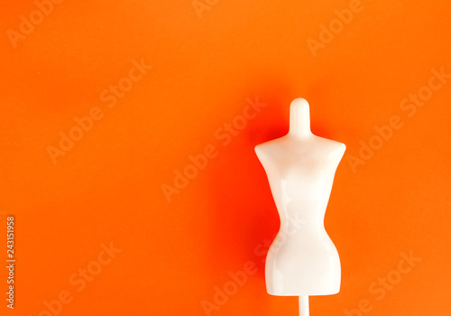 White plastic female mannequin figure on bright orange background