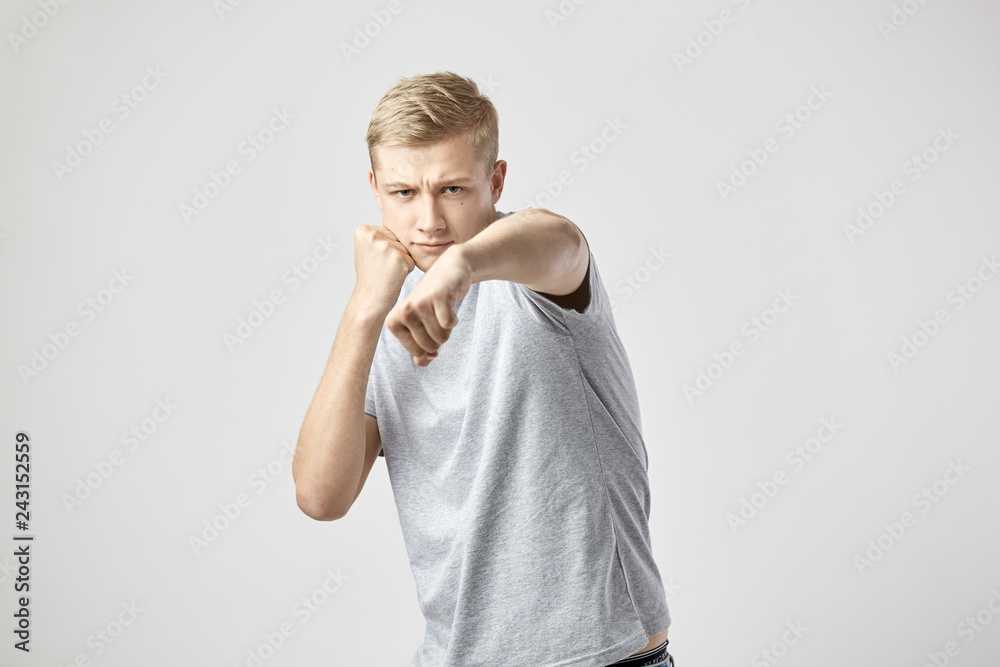 Blond guy dressed in a white t-shirt and jeans holds hands in fists on the white background in the studio Blond guy dressed in a white t-shirt and jeans holds hands in fists on the white background in the studio