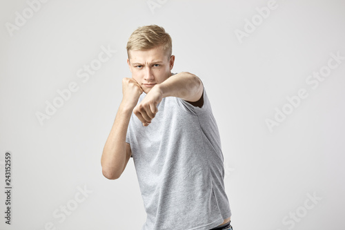 Blond guy dressed in a white t-shirt and jeans holds hands in fists on the white background in the studio