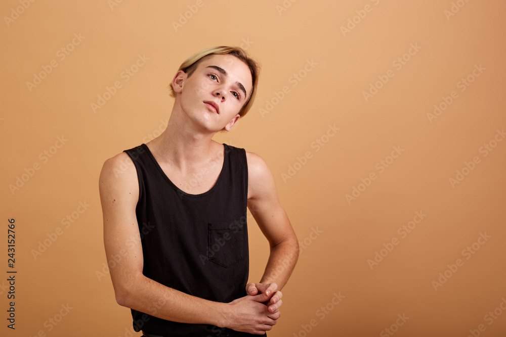 Young skinny blond guy dressed in a black tank top and pants posing in the  studio on the beige background Stock Photo | Adobe Stock