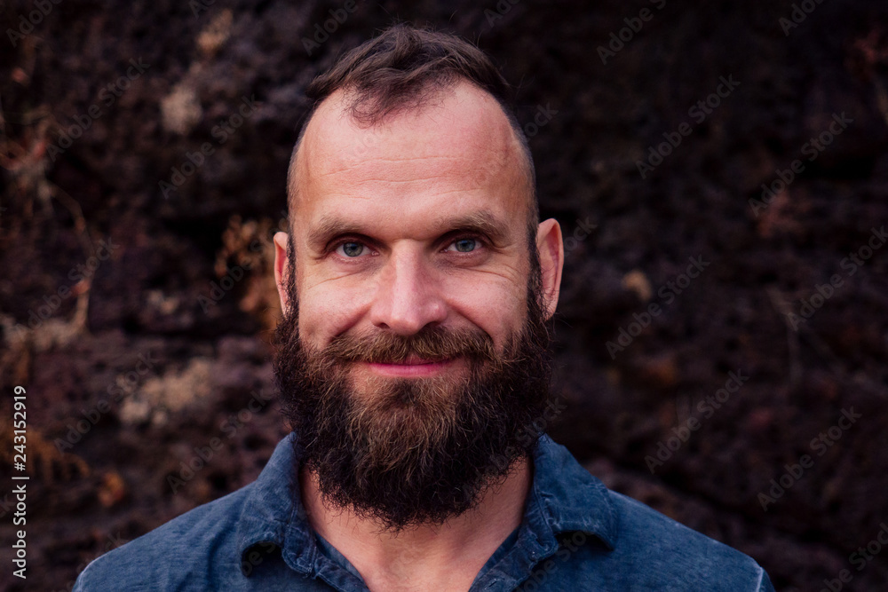 Fototapeta premium Handsome man with beard. Close up portrait of stylish bearded hipster on stoun roks beach background. Attractive young person toothy smile face beard festival. shaving idea.