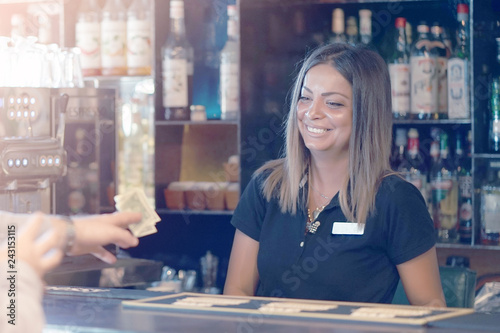 The waiter girl receives a tip from the client at the hotel bar. The girl is happy with luck. A bartender woman is happy to receive a tip at work. Emotions. The concept of service. Toning
