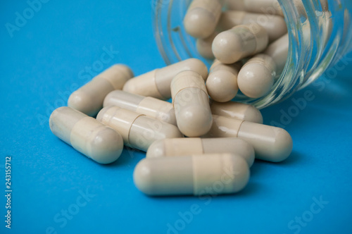 closeup of beige capsules falling from glass container on blue background