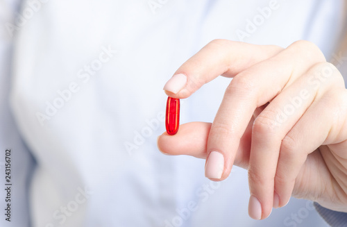 Red capsule pill medicine in woman hand on blur background, pharmacy concept