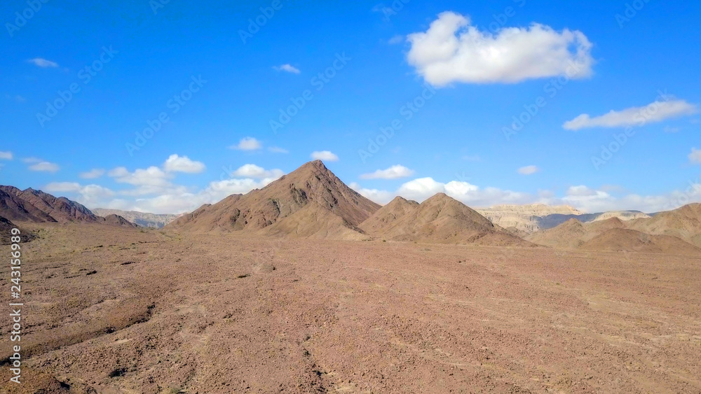Desert landscape - Aerial image of mountains and dry land with blue cloudy sky in the background.