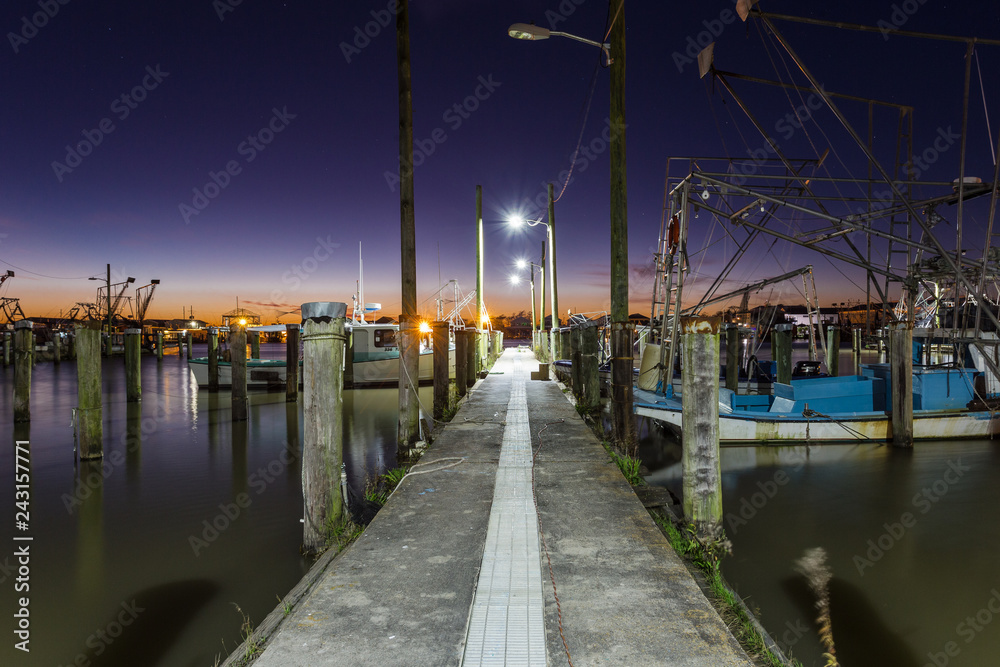 Old vintage dock were tired shrimp boats wait to go to work on calm water with deep purple and orange sunset