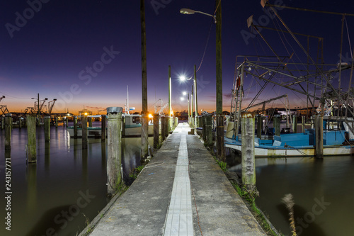 Old vintage dock were tired shrimp boats wait to go to work on calm water with deep purple and orange sunset