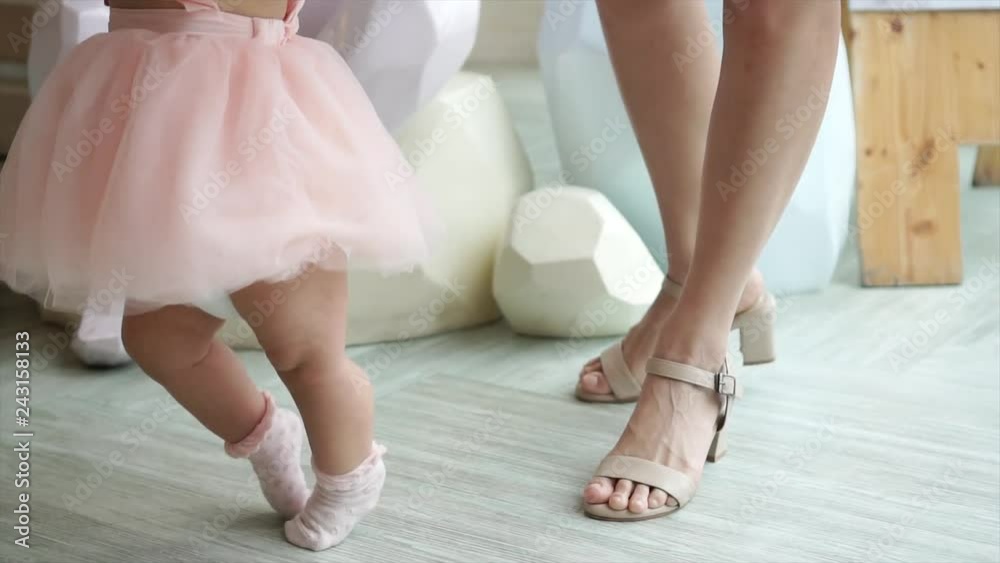 Feet of toddler baby taking first steps with mother help at special event like wedding or birthday party Feet of toddler baby taking first steps with mother help at special event like wedding or birthday party