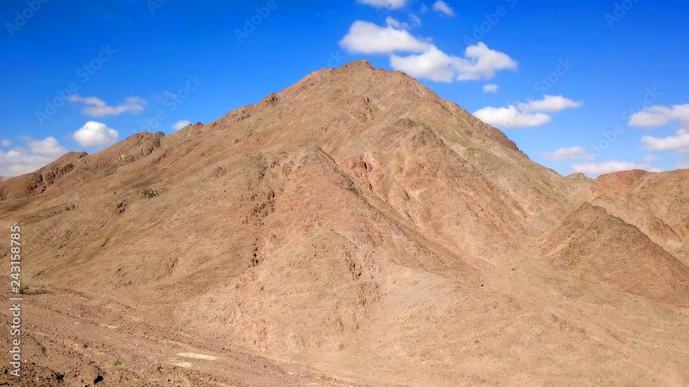 Desert landscape - Aerial image of mountains and dry land with blue cloudy sky in the background.