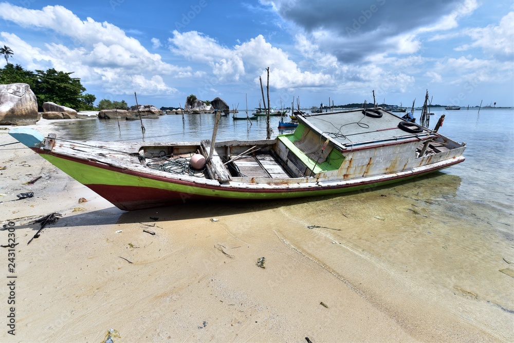 Weathered fishing boat lying on a sandy beach Pantai Tanjung Kelayang on the Island of Belitung, Indonesia