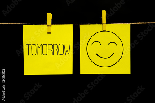Copy space. Two yellow stickers. On left a sheet inscription tomorrow. On the right sheet face with smile and good nature. Emotion.