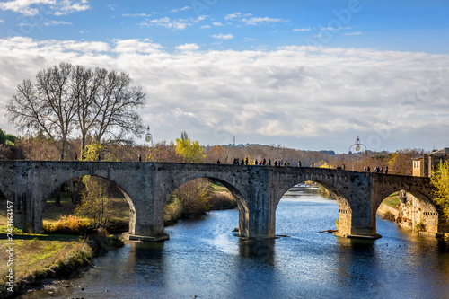 Tourist and locals crossing a old stone bridge over a calm river in Carcassonne in France