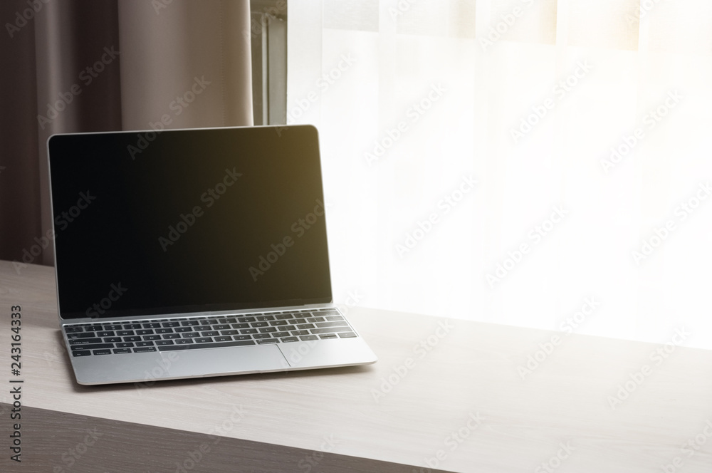 Fototapeta premium Modern laptop lay on wooden table next to white curtain in morning, freelancer and blogger notebook work from home.